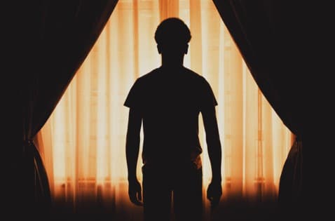 What is the meaning of the dark night of the soul? Image ofman silhouetted against an orange curtain.