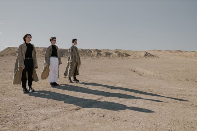 The Meaning of the Dark Night of the Soul - photo of 3 people in trenchcoats standing in the desert with long shadows.