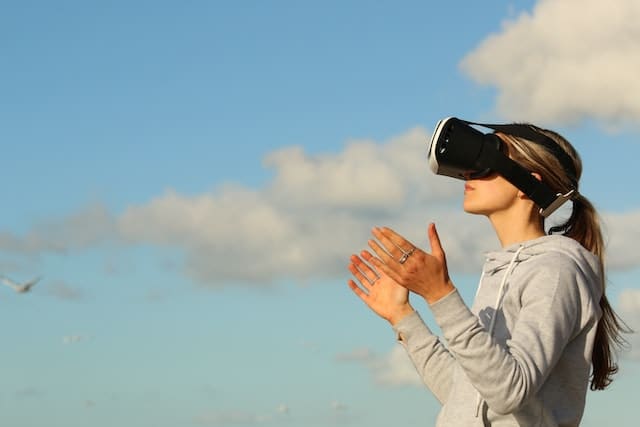 Woman in a virtual reality headset against a blue sky with clouds.
