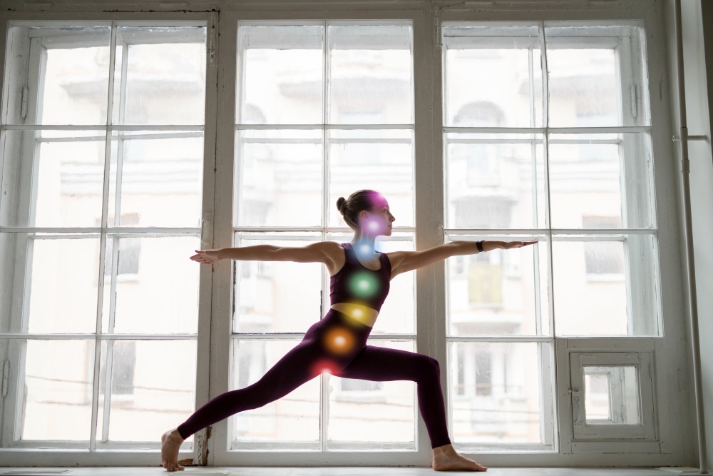 Woman doing yoga with the seven chakras represented as coloured lights on her body.