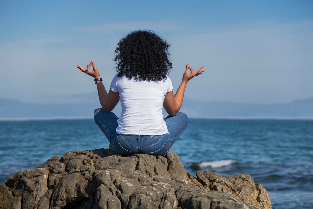 How to have a spiritual awakening: woman in yoga pose on a rock looking out to sea.