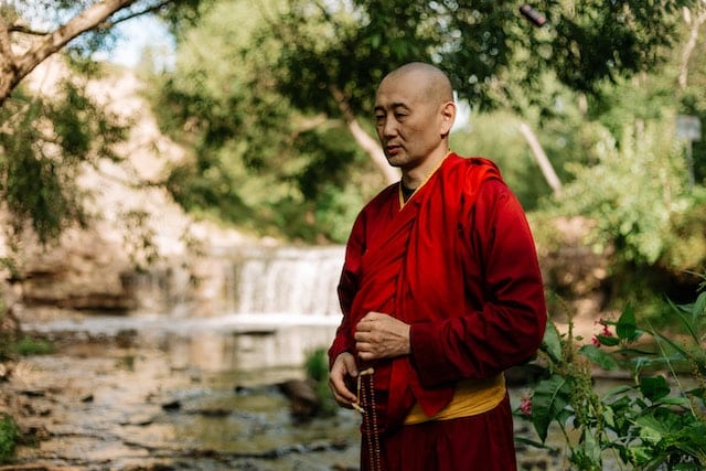 Why does spiritual awakening happen: a buddhist monk in red robes in a tranquil landscape.