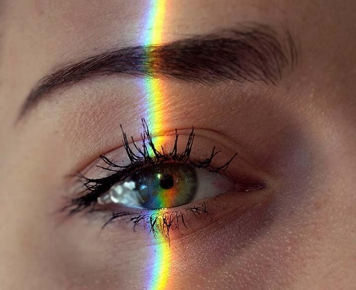 Why does spiritual awakening happen: woman's eye with a stripe of rainbow light reflected through it.