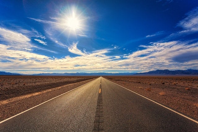 Road stretching into the distance, with a bright blue sky and sun