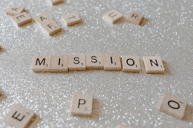 The word mission spelled out in wooden tiles on a sparkly silver background.