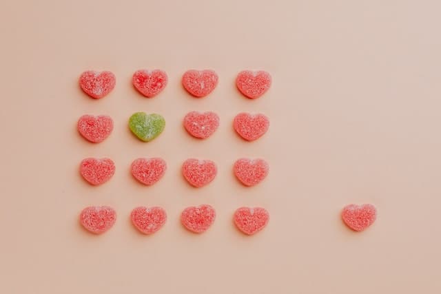 One green heart-shaped sweet amongst a grid of red heart-shaped sweets