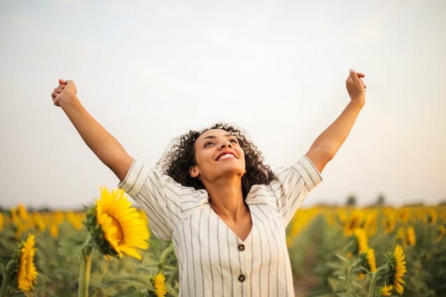 Smiling woman raising her arms to the sky in a field of sunflowers.