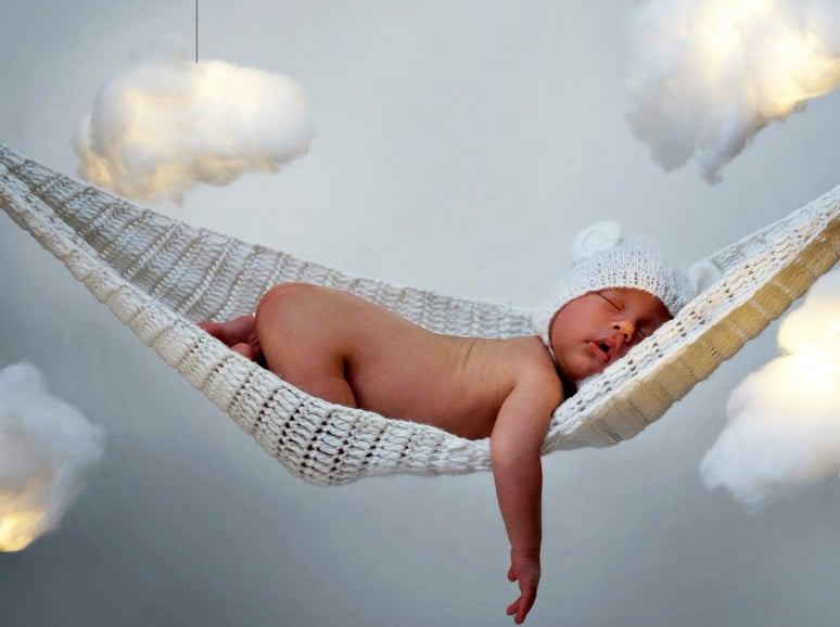 Spiritual meaning of dreams about babies: baby fast asleep in a hammock with cotton wool clouds in the background.
