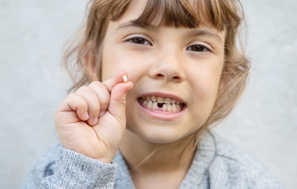 Teeth falling out dream spiritual meaning: little girl with a gap in her teeth holding a baby tooth.