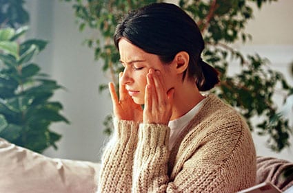 10 Physical symptoms of spiritual awakening: woman sitting on sofa holding her temples as though she has a headache.